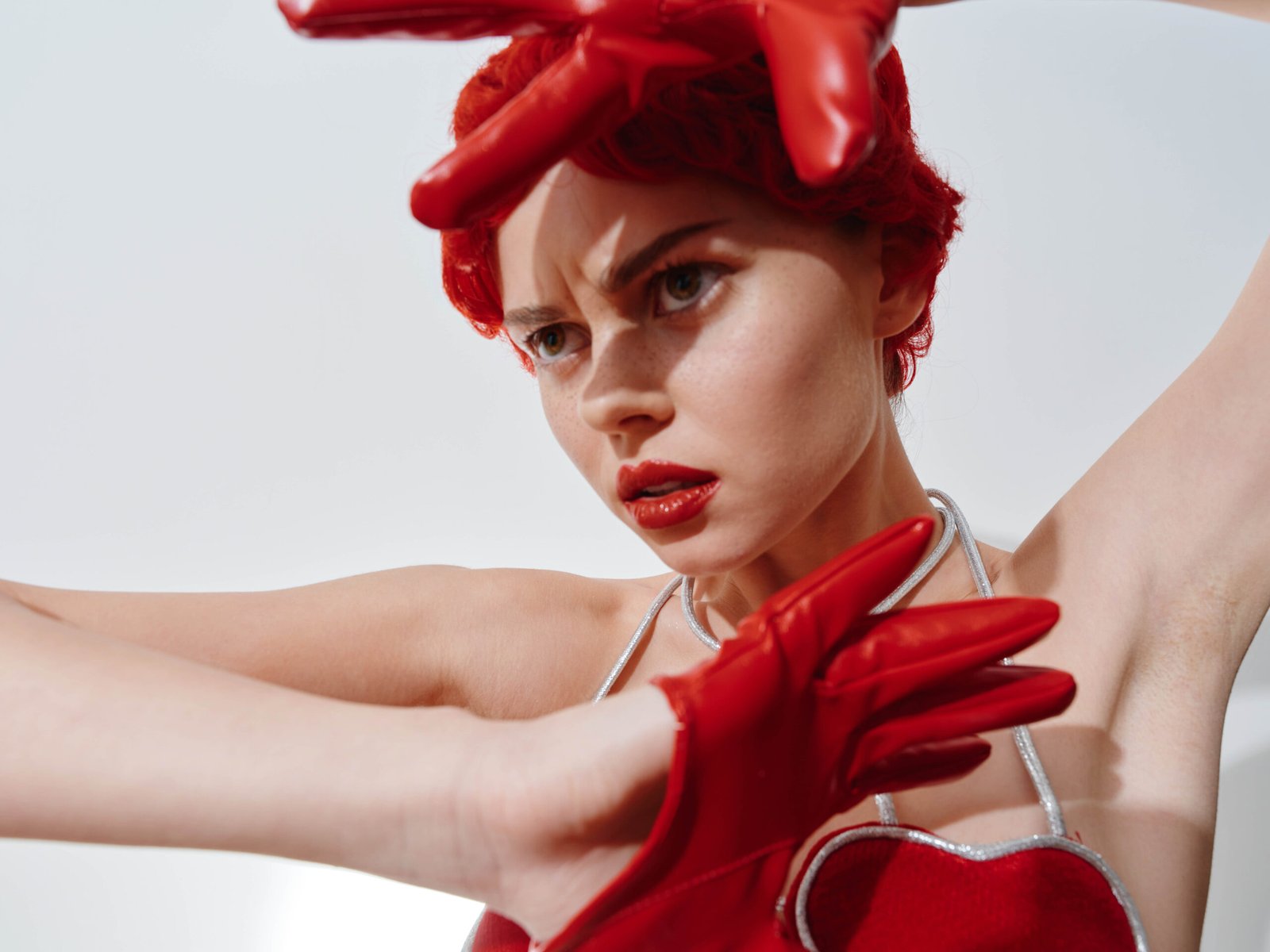Beautiful woman with red hair and gloves posing with hands in front of face in studio photoshoot